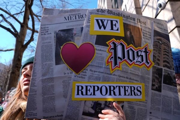 Плакат с надписью "WE ♥ Post REPORTERS" на фоне здания и деревьев.