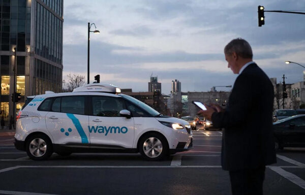 Автомобиль Waymo на городском перекрестке при свете вечерних фонарей.