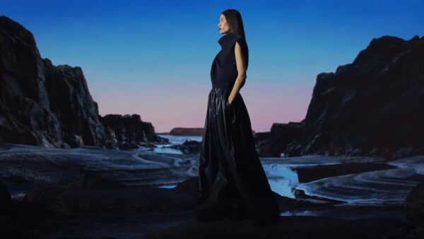 Женщина в длинном платье позирует на фоне скалистой местности на закате.