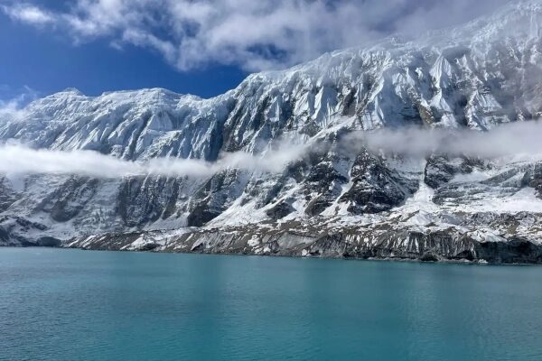 Снежные горы и бирюзовое озеро под облаками, живописный пейзаж.