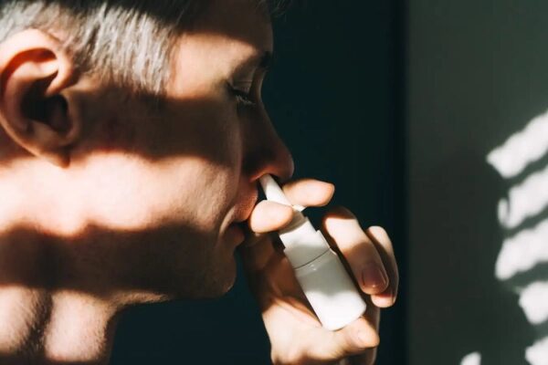Мужчина использует назальный спрей для облегчения симптомов насморка.