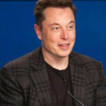 Мужчина в костюме с микрофоном на фоне синего экрана на конференции.