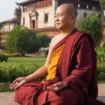 Монах в медитации на фоне древнего храма и зелени.