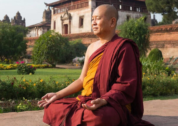 Монах в медитации на фоне древнего храма и зелени.