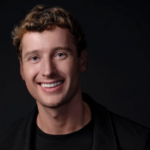 Улыбающийся мужчина в черной одежде на темном фоне.