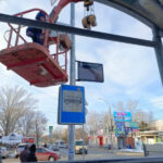 Рабочий в подъёмнике устанавливает знак на автобусной остановке зимой.