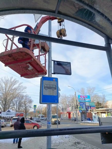 Рабочий в подъёмнике устанавливает знак на автобусной остановке зимой.