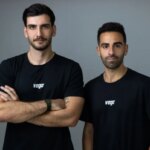 Два человека в черных футболках с логотипом "vego" на сером фоне.