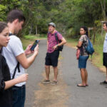 Группа людей в походе на лесной тропе, один из них смотрит в телефон.