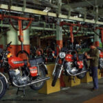 Мотоциклы на конвейере завода, рабочий осматривает красные байки в сборочном цеху.