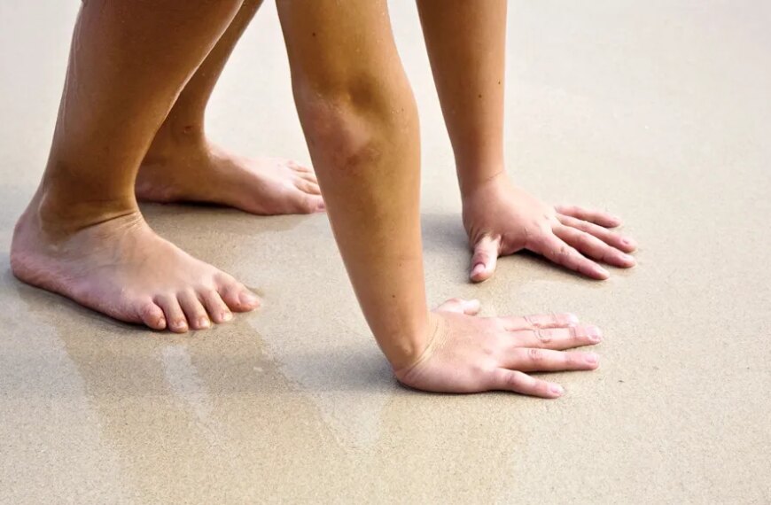 Человек на песчаном пляже, стоящий на четвереньках, босые ноги и руки на песке.