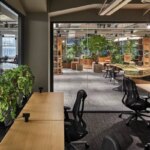 Современный офис с зелеными растениями, стеклянными стенами и стильными рабочими местами.