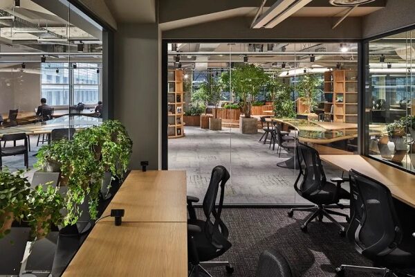 Современный офис с зелеными растениями, стеклянными стенами и стильными рабочими местами.