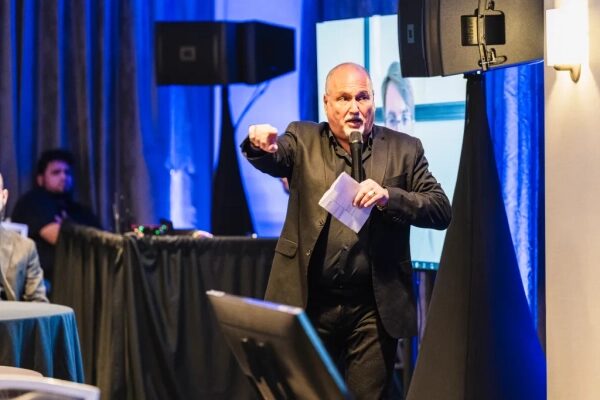 Человек в костюме проводит презентацию на конференции с экраном и аудиторией.