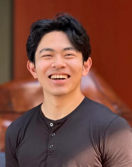 Молодой человек в черной футболке улыбается на улице.