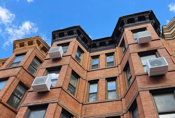 Красно-кирпичное здание с кондиционерами на фоне голубого неба.