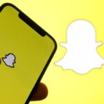 Смартфон с логотипом Snapchat на экране на фоне желтого логотипа-призрака.