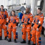 Четыре человека в оранжевых космических скафандрах стоят рядом с космической капсулой Artemis.
