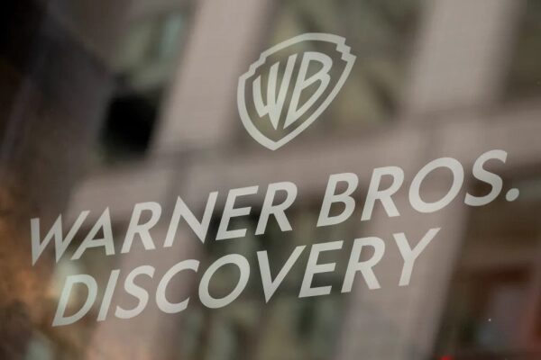 Логотип Warner Bros Discovery на стеклянной двери, отражающий здания на заднем плане.