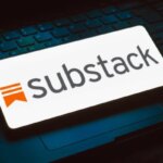 Логотип Substack на экране смартфона, лежащем на клавиатуре ноутбука.