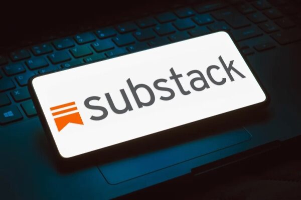 Логотип Substack на экране смартфона, лежащем на клавиатуре ноутбука.