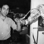 Человек управляет роботизированной рукой в лаборатории, черно-белое фото.