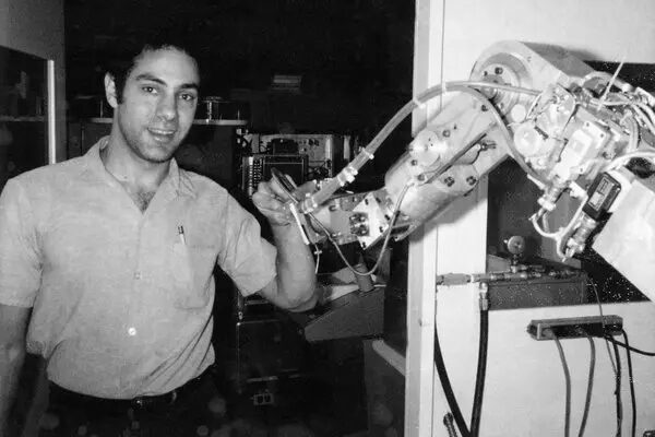 Человек управляет роботизированной рукой в лаборатории, черно-белое фото.