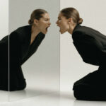 Женщина в черном костюме смотрит в зеркало, создавая интересный визуальный эффект.