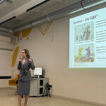 Презентация в офисе: женщина в костюме выступает перед экраном с слайдом о Колоссе.