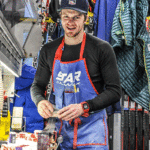 Мастер обрабатывает лыжи в мастерской, окружен снаряжением и инструментами для ухода.