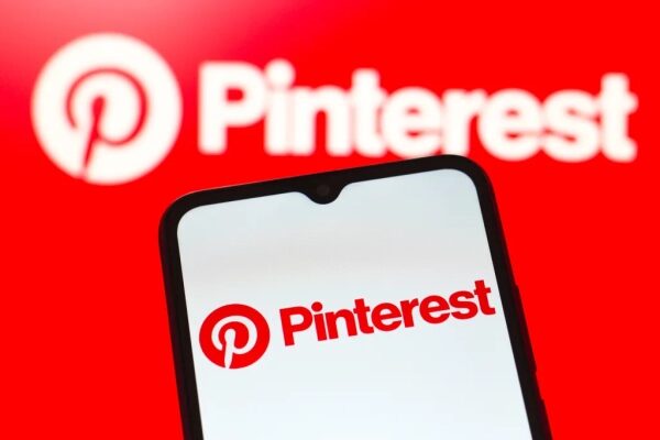 Смартфон с логотипом Pinterest на фоне ярко-красного логотипа на экране.
