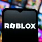 Логотип Roblox на экране смартфона с размытым фоном из иконок игр.