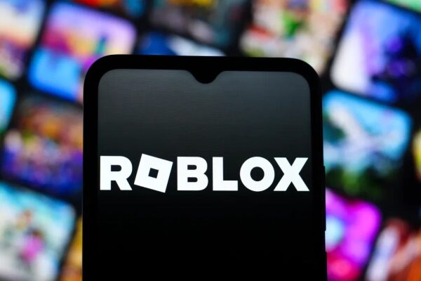 Логотип Roblox на экране смартфона с размытым фоном из иконок игр.