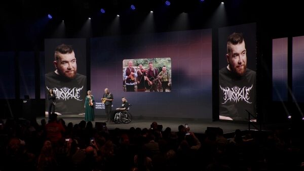 Презентация на сцене с фотопортретами мужчины и группы людей.