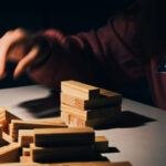 Человек играет в дженгу, рука над деревянными блоками на столе.