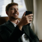 Человек в офисе смотрит в смартфон, сидя в кожаном кресле у окна.