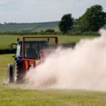 Трактор в работе на поле, поднимающий пыль, сельскохозяйственный пейзаж летом.