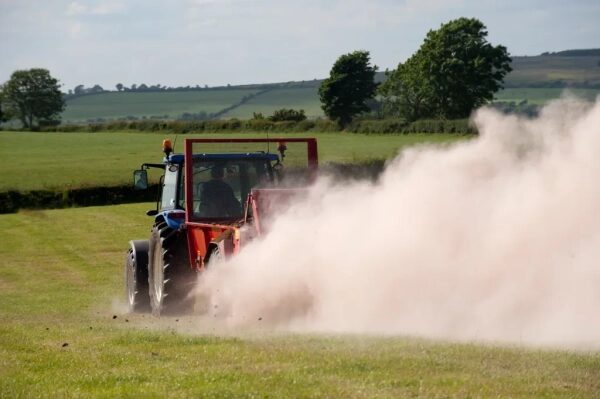 Трактор в работе на поле, поднимающий пыль, сельскохозяйственный пейзаж летом.