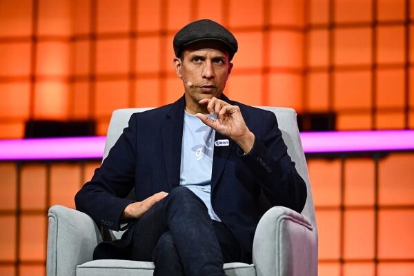 Мужчина в шляпе и пиджаке сидит в кресле на конференции.