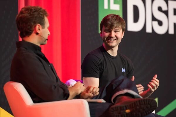 Два человека обсуждают на технологической конференции, сидя на сцене.