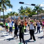 Группа людей танцует на улице под пальмами при солнечной погоде.