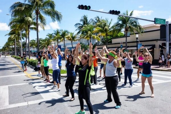 Группа людей танцует на улице под пальмами при солнечной погоде.