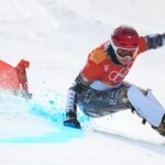 Сноубордист на зимней Олимпиаде 2022, скоростной спуск на фоне олимпийского флага.