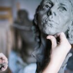 Скульптор формирует голову из глины руками в мастерской. Искусство лепки и творчество.