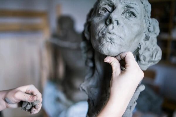 Скульптор формирует голову из глины руками в мастерской. Искусство лепки и творчество.