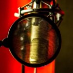 Микрофон с поп-фильтром на красном фоне для звукозаписи.