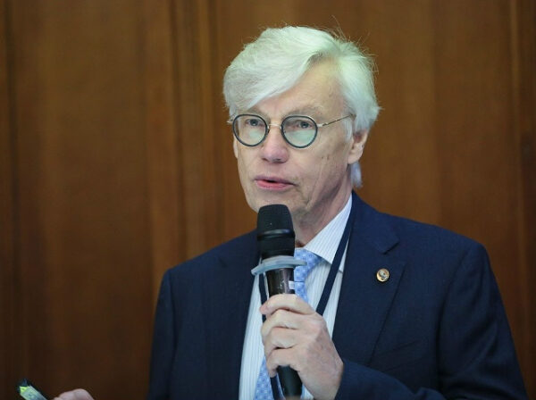 Радиохимия, СКИФ, биокатализ и не только. На химическом факультете МГУ впервые проходит конференция ChemNet 3 Мужчина в очках и костюме говорит в микрофон на фоне деревянной стены.