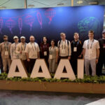 Группа людей на конференции AAAI, баннер с фонариками и львом на заднем плане.