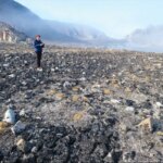 Человек на скалистой равнине с горами на заднем плане, ясное утро.