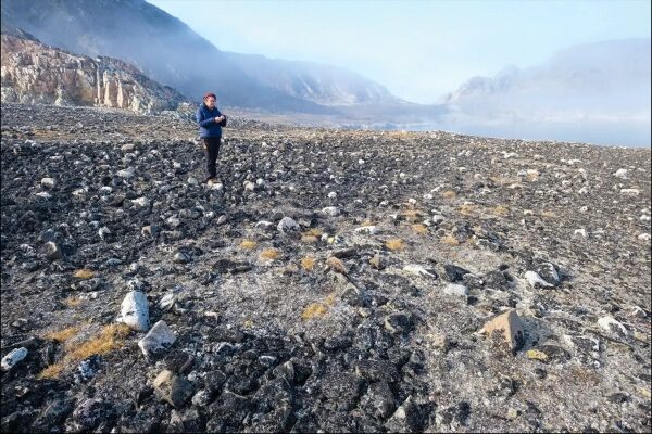 Человек на скалистой равнине с горами на заднем плане, ясное утро.